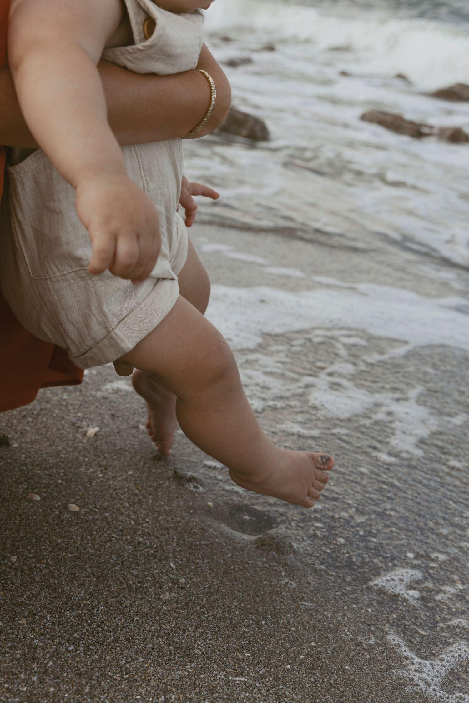 Close-up of baby's feet touching ocean water on sandy beach.
