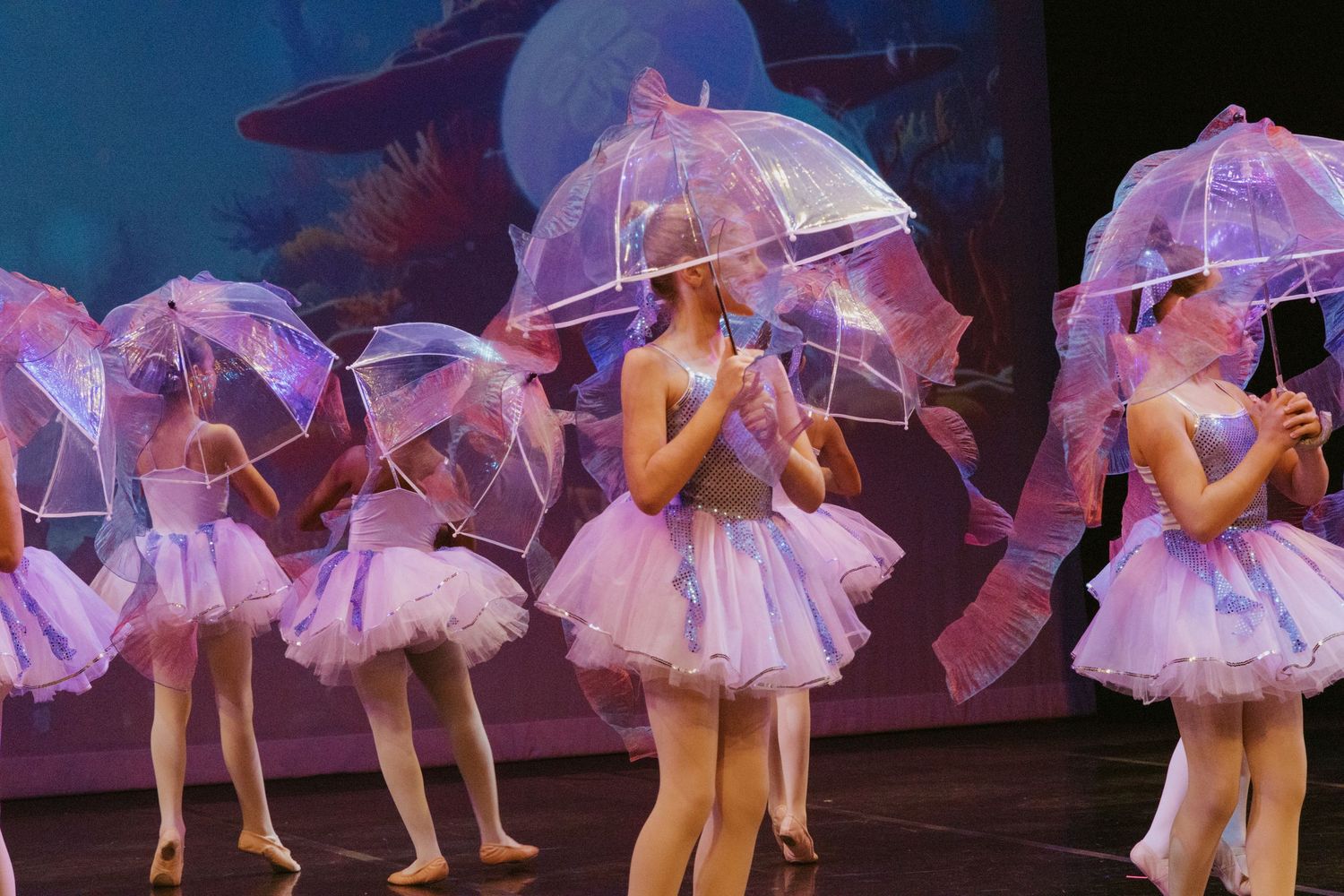 Ballet performers in white tutus hold clear umbrellas during a stage production.