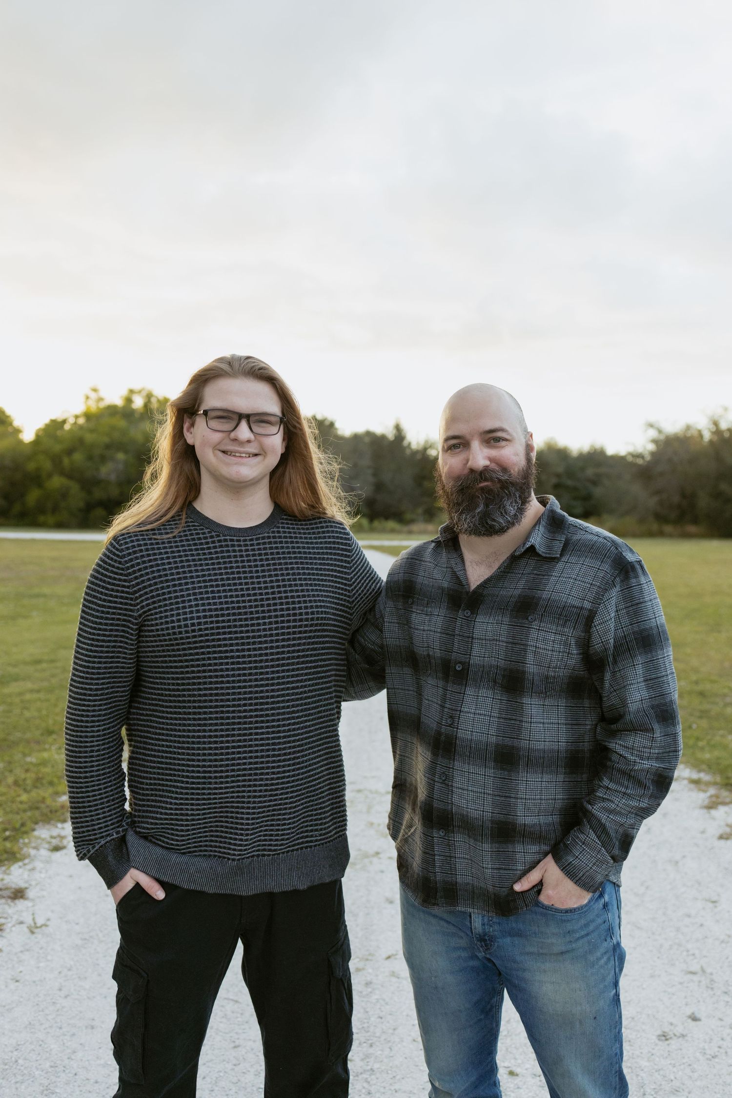 Two friends stand together outdoors wearing casual winter clothing at sunset.