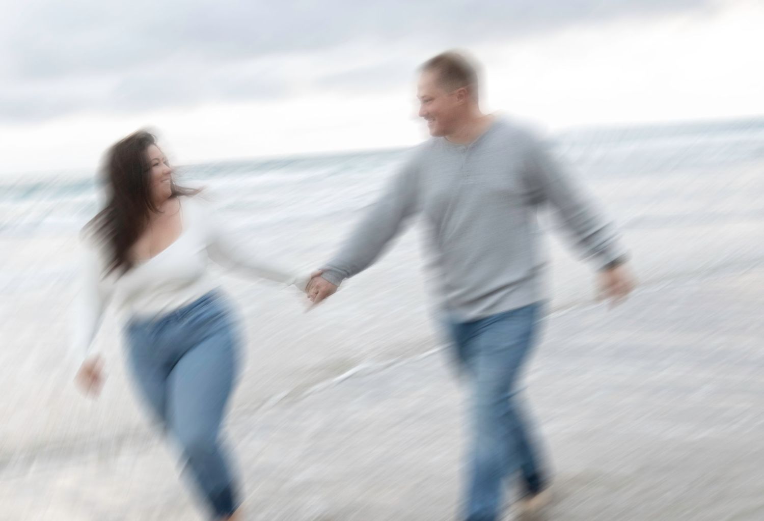 Blurred motion capture of a couple running and laughing by the ocean.