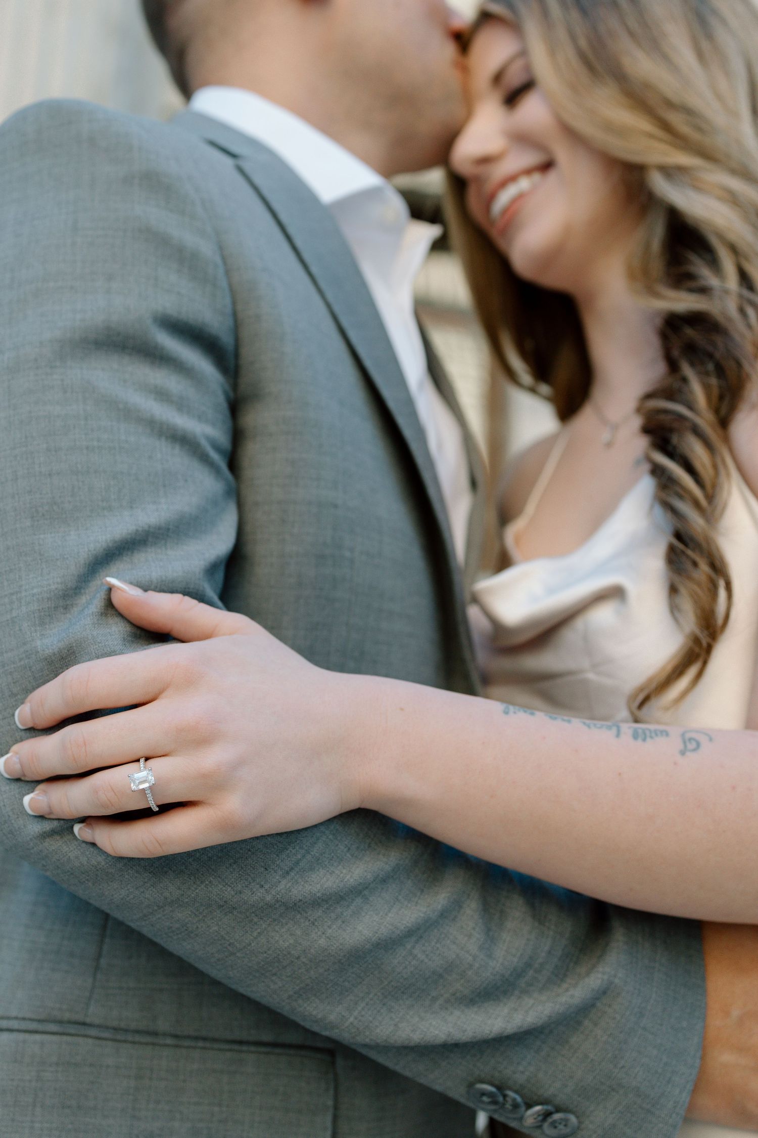 Close-up of couple embracing showing engagement ring and elegant formal attire.