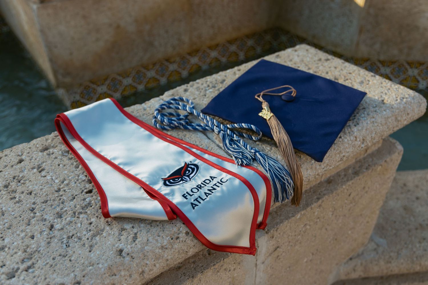 Graduation cap and stole arranged on a concrete surface in natural lighting.
