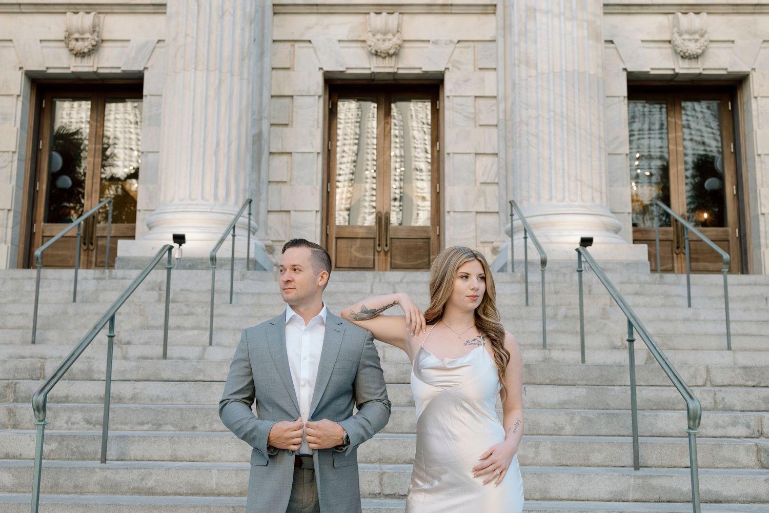 Wedding couple poses back to back on grand steps of classical building.