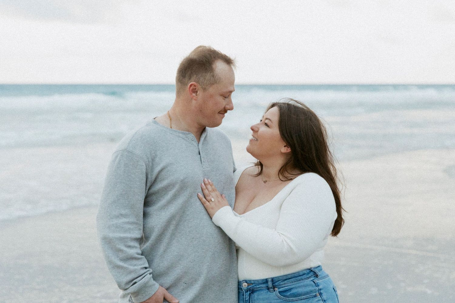 A loving couple shares a tender moment together on a misty beach wearing casual sweaters.