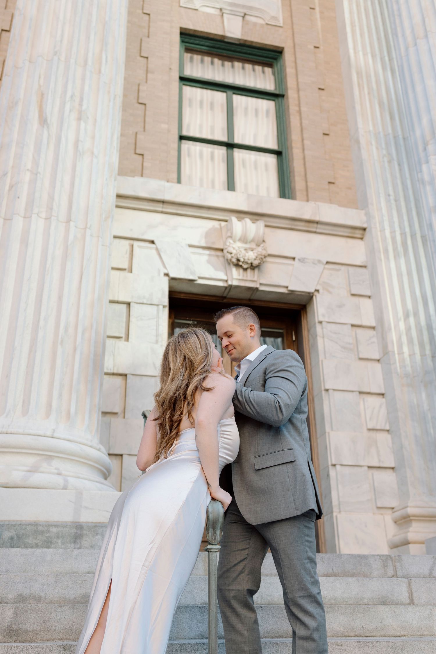 Couple in formal attire embraces by classical column architecture.