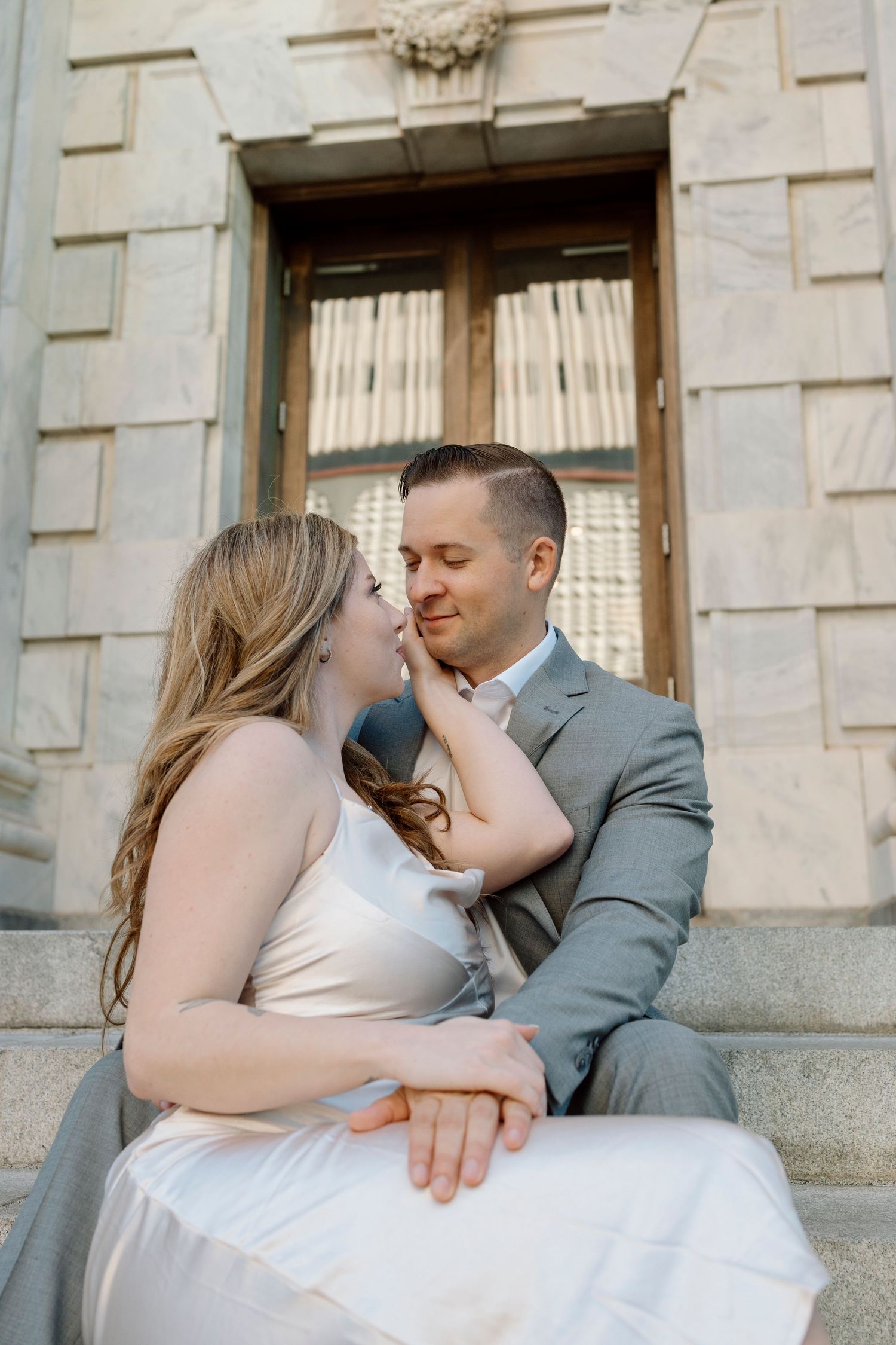 Romantic wedding couple sitting on stone steps share an intimate moment in front of an ornate doorway.