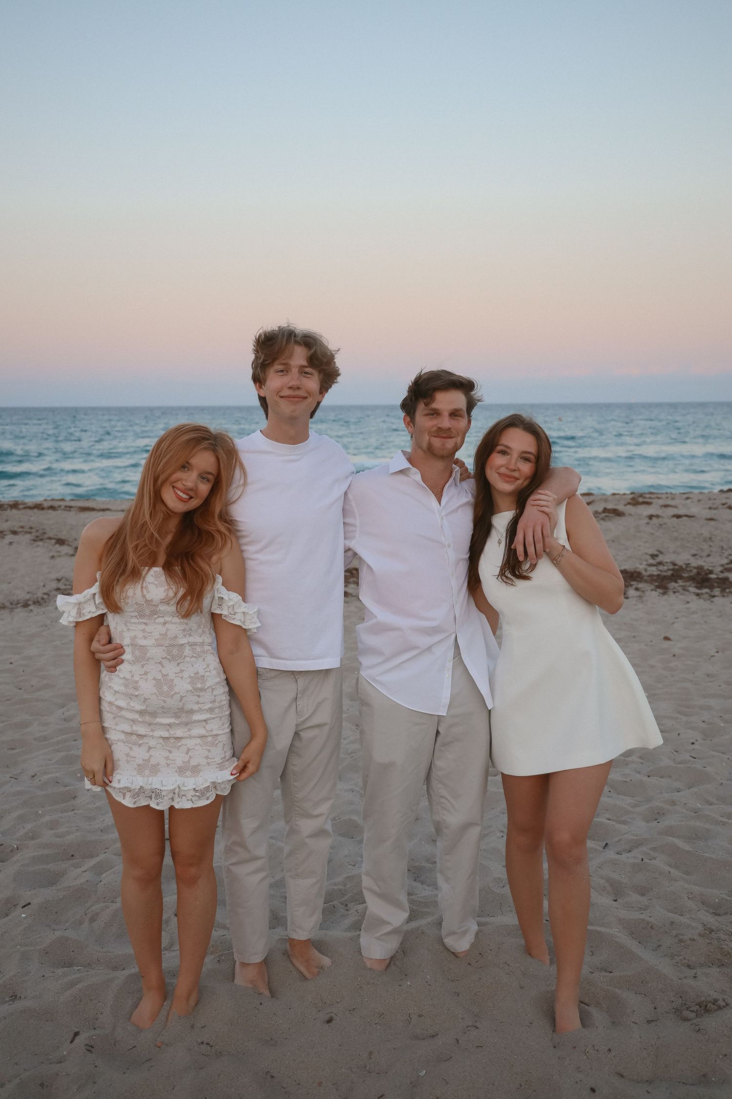 Beach portrait of four people in white outfits standing together at sunset.