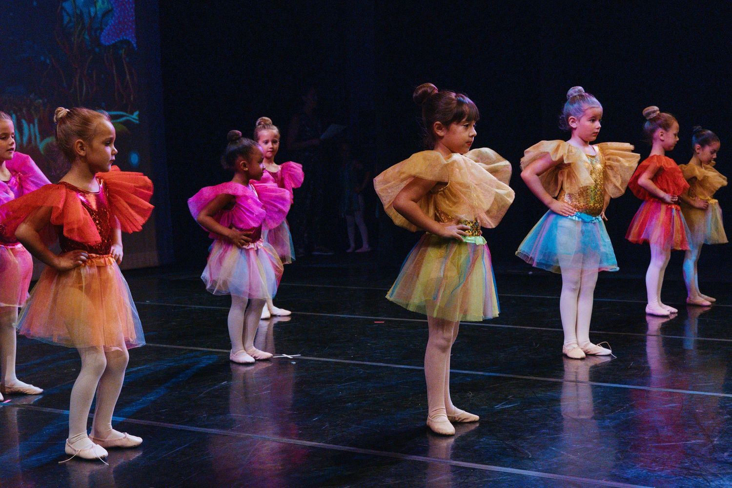 Young ballet dancers in pastel tutus practice positions during a dance recital.