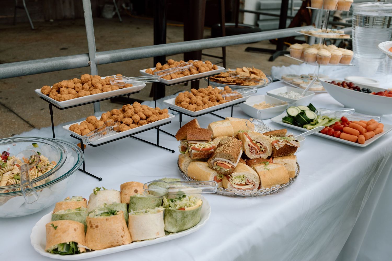 Catered buffet spread featuring sandwiches, wraps, fresh vegetables, and finger foods arranged on tiered platters and serving plates.