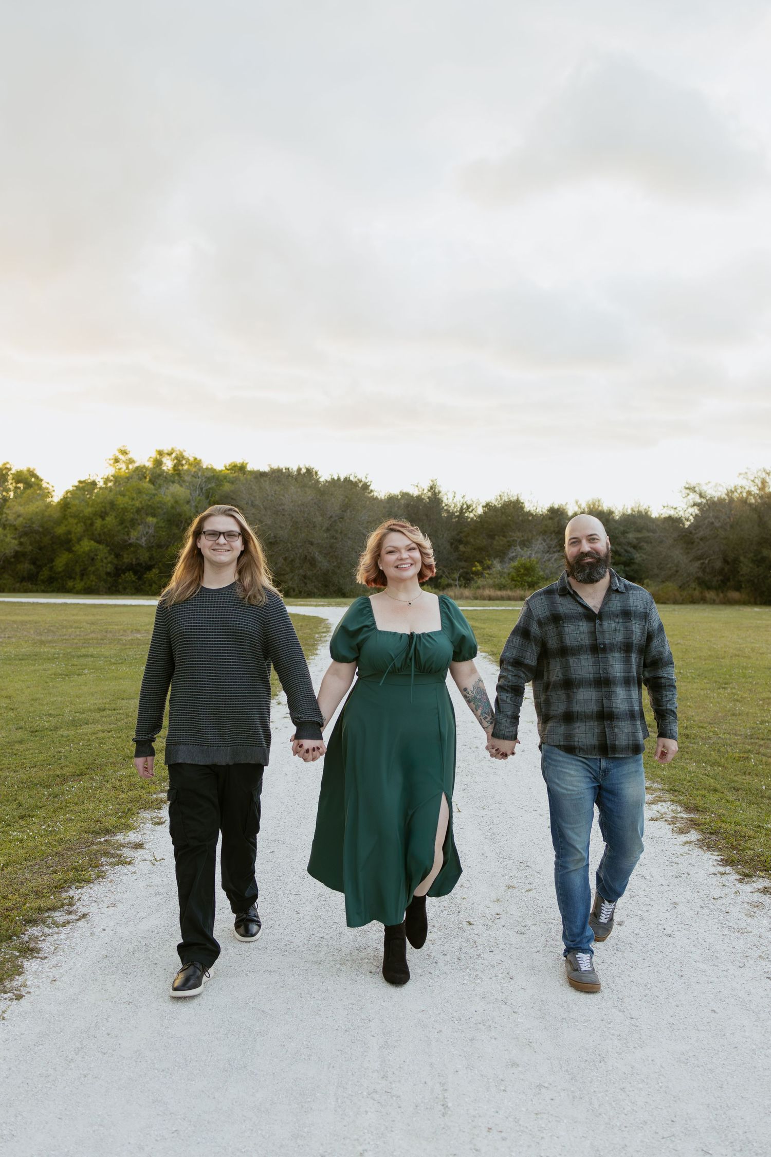 Three people walking together on a white gravel path through a green field at sunset.