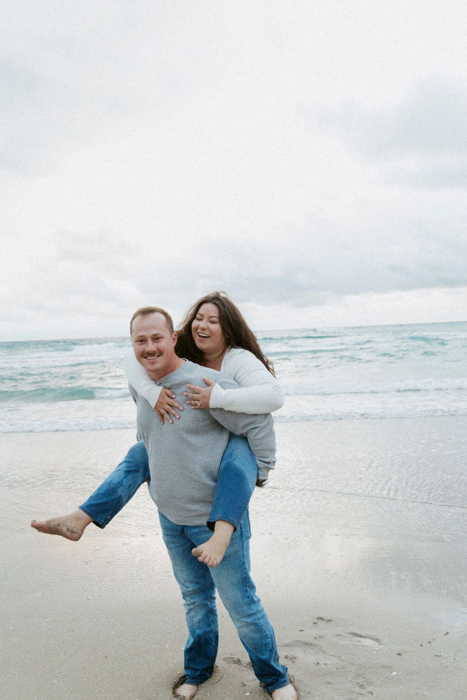 Playful piggyback ride on beach with ocean waves in background.