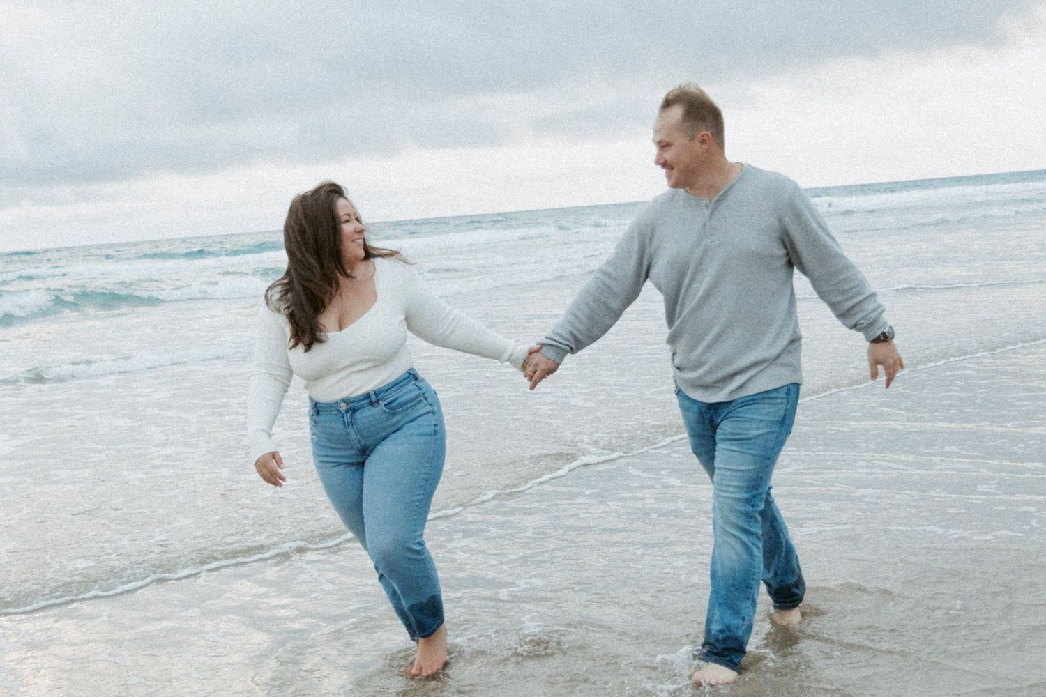 Couple holding hands and dancing together joyfully on a cloudy beach.