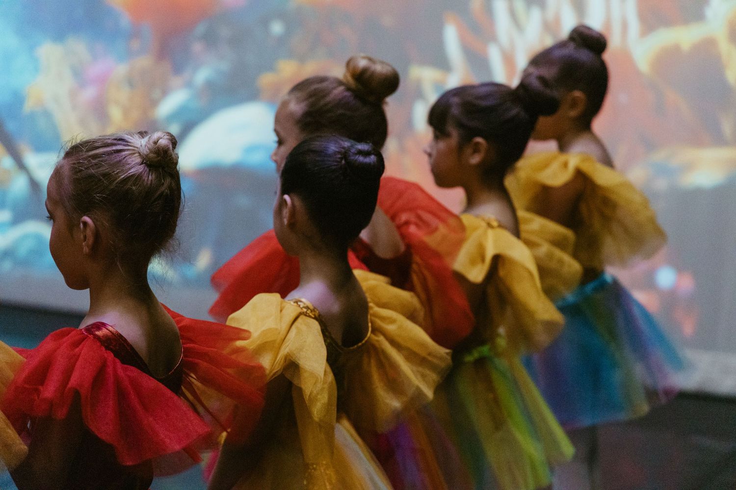 Dancers wearing red and yellow tutus stand in formation during a stage performance.