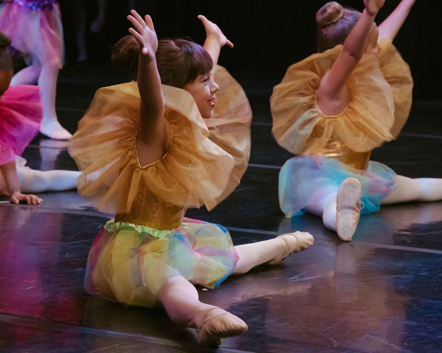 Dancers in peach-colored tutus perform graceful floor movements during a ballet recital.