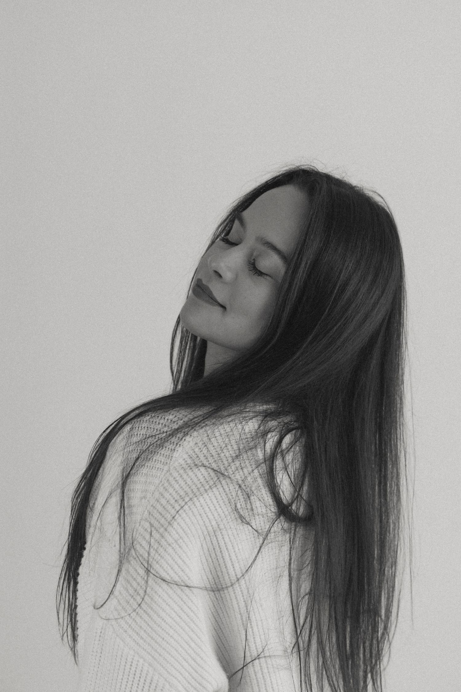 Artistic black and white portrait of woman with flowing dark hair in contemplative pose.