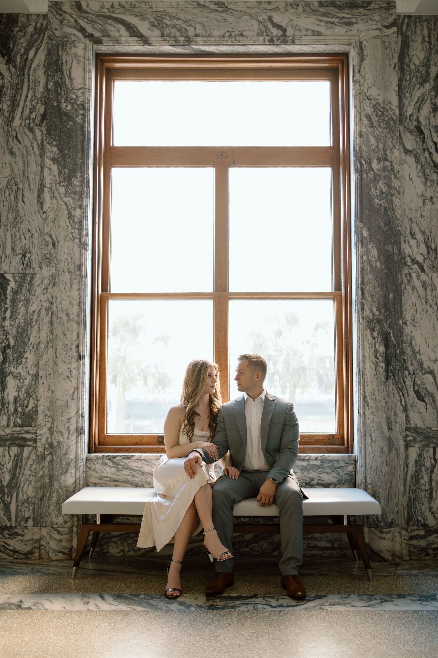 Elegantly dressed couple sits on marble windowsill sharing a romantic moment.