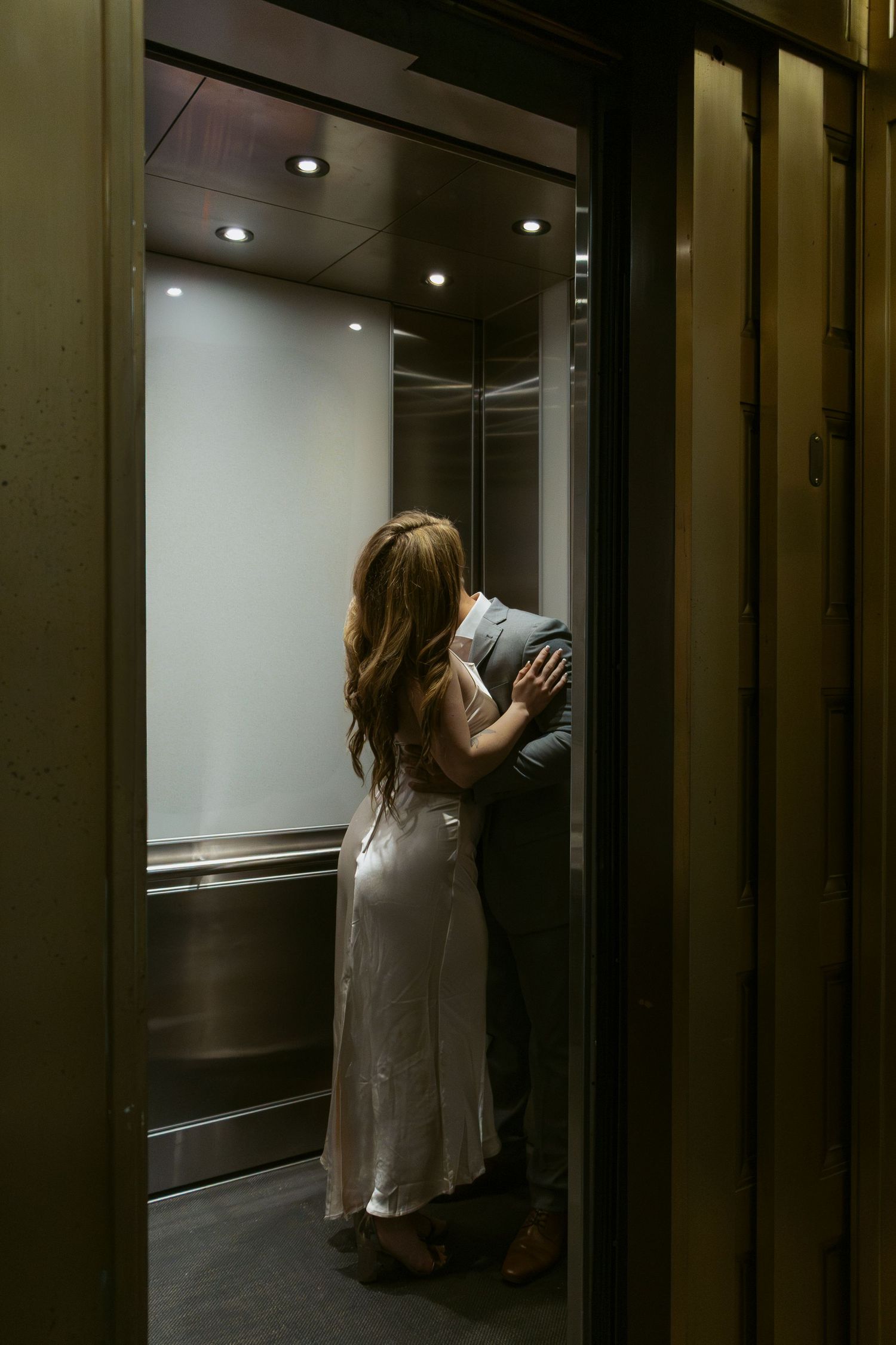 Couple shares intimate moment in dimly lit elevator.