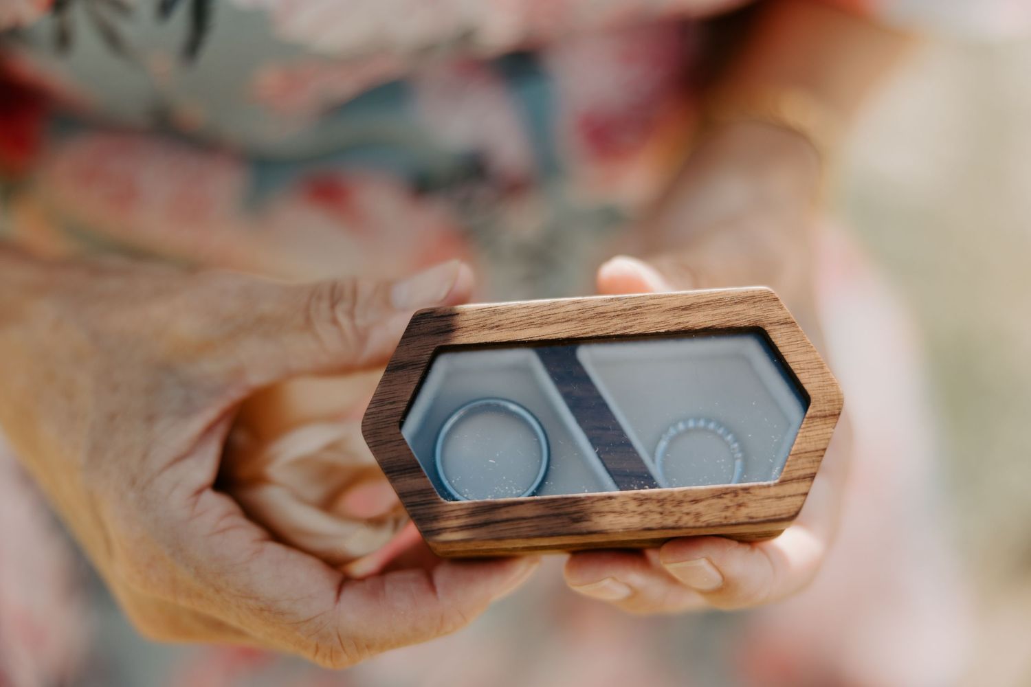 Wooden ring box with two wedding bands held in hands.