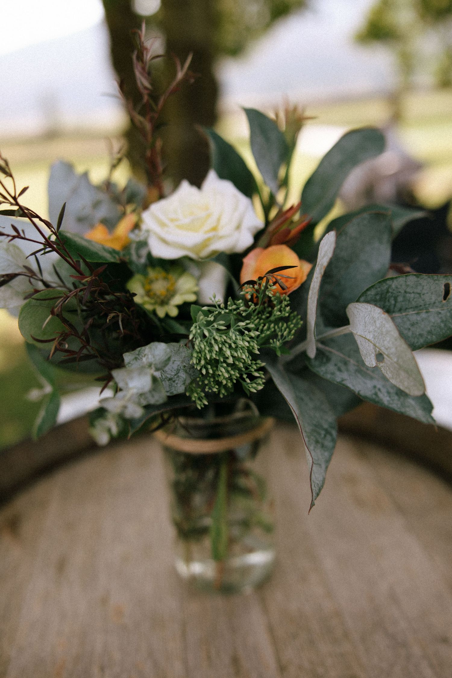 An elegant wedding centerpiece with white roses and mixed greenery in a glass vase.