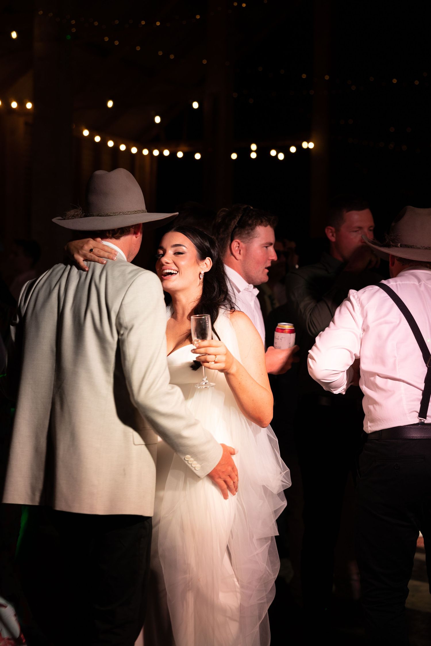 A couple shares a joyful moment dancing together under strings of twinkling lights at an evening celebration.