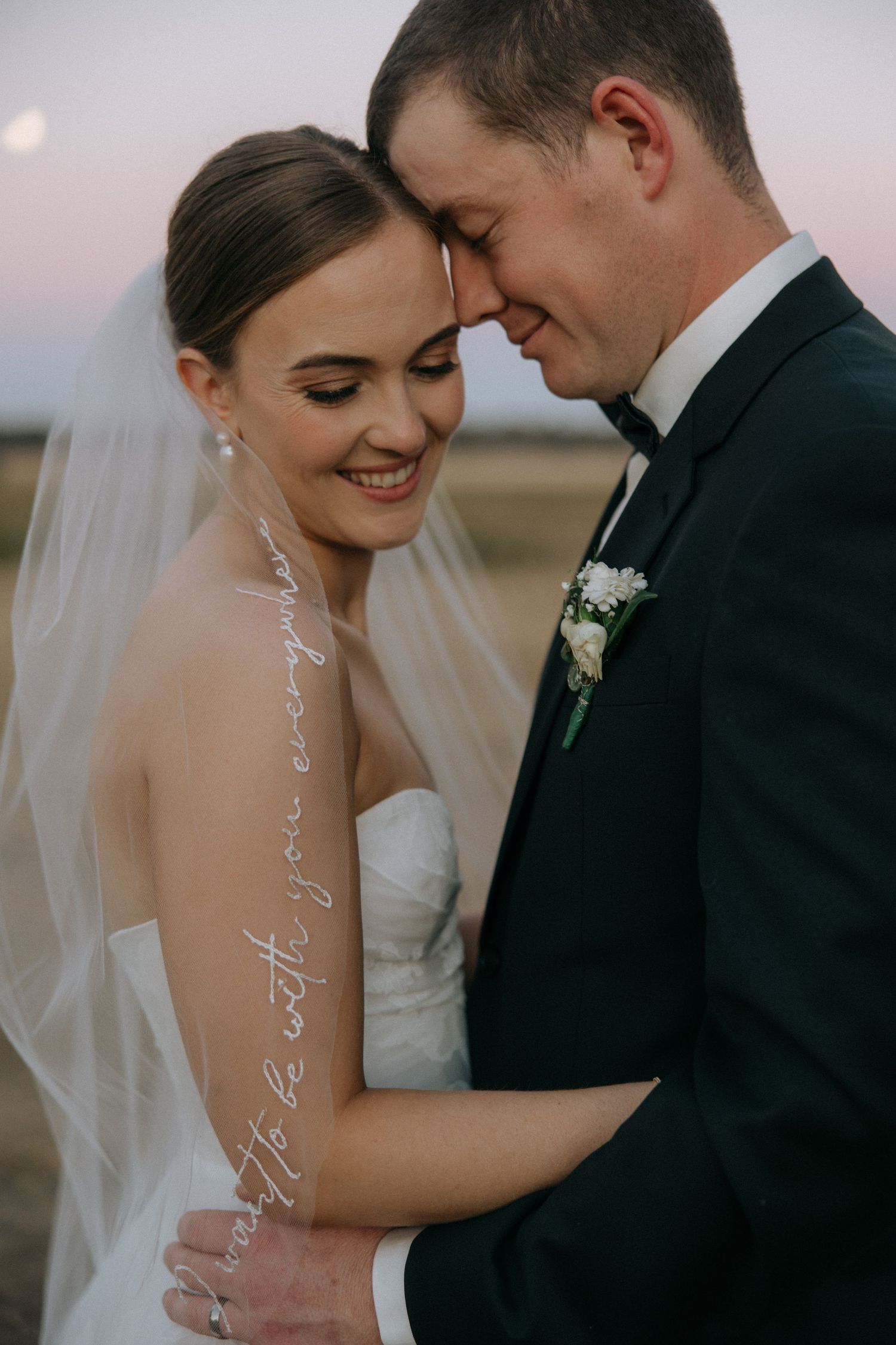 Intimate moment between newlyweds with bride wearing delicate veil at sunset.