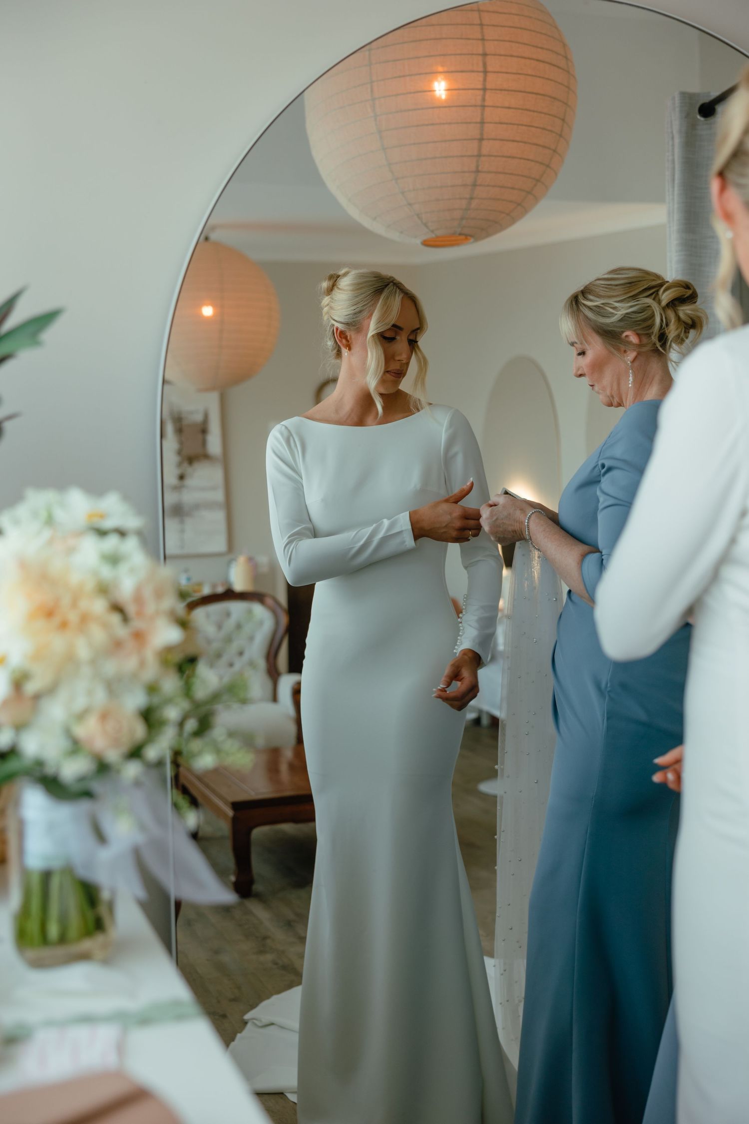 Wedding dress fitting in bright room with peach paper lantern and floral arrangements.