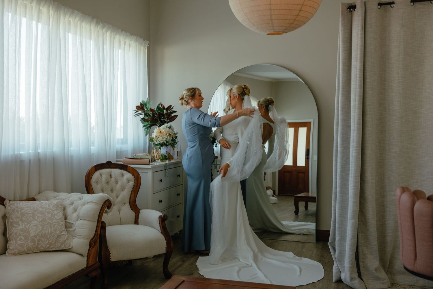 Wedding dress preparations in sunlit room with vintage furniture and paper lantern.