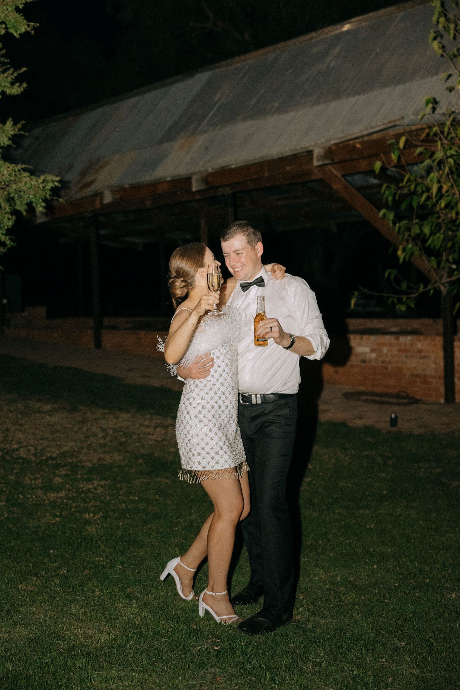 A couple shares a joyful dance moment under an open-air pavilion at night during wedding celebrations.