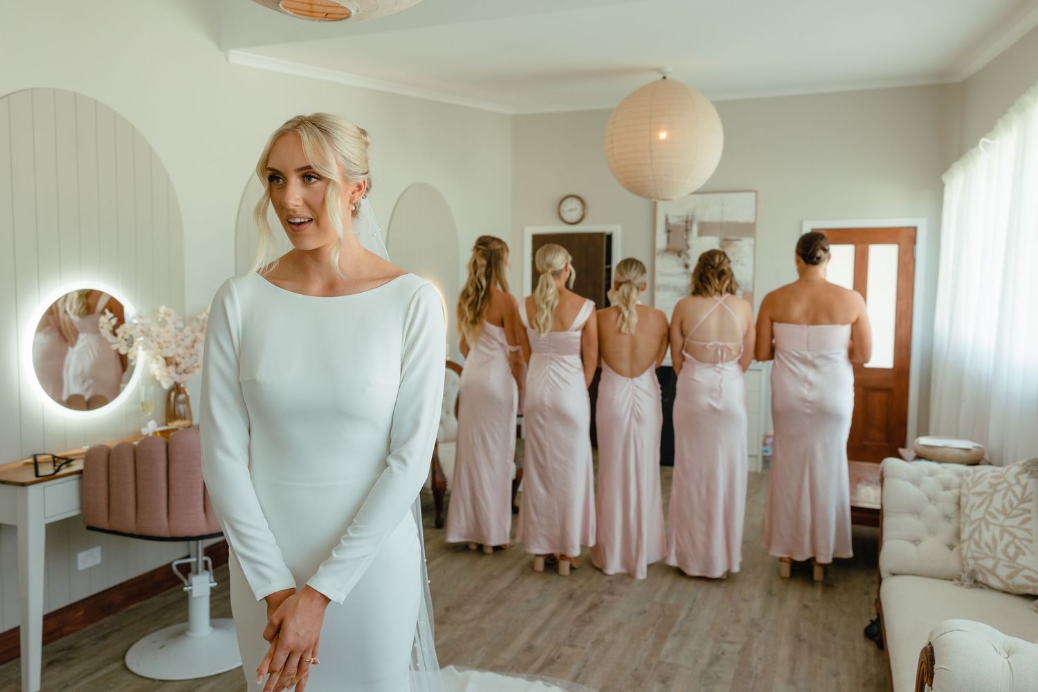 Elegant wedding preparations with bridesmaids in blush dresses and paper lantern lighting.