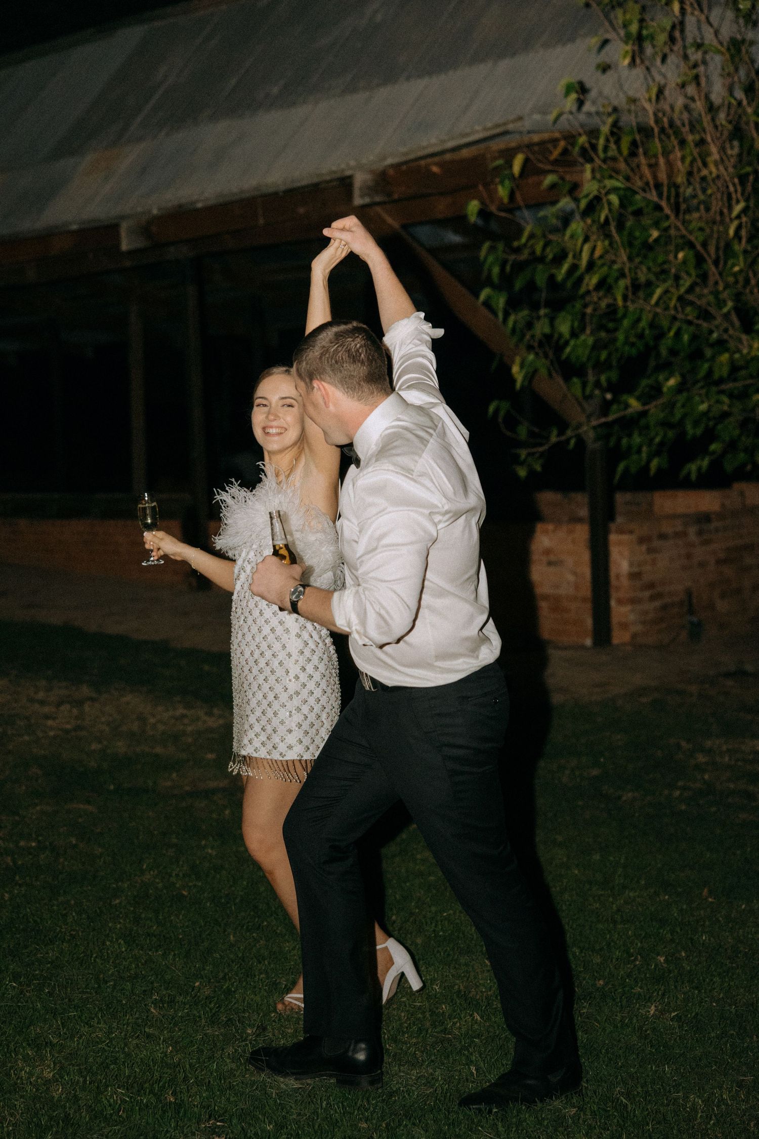A couple dances together on a grassy lawn at night, with one person twirling the other during a celebration.