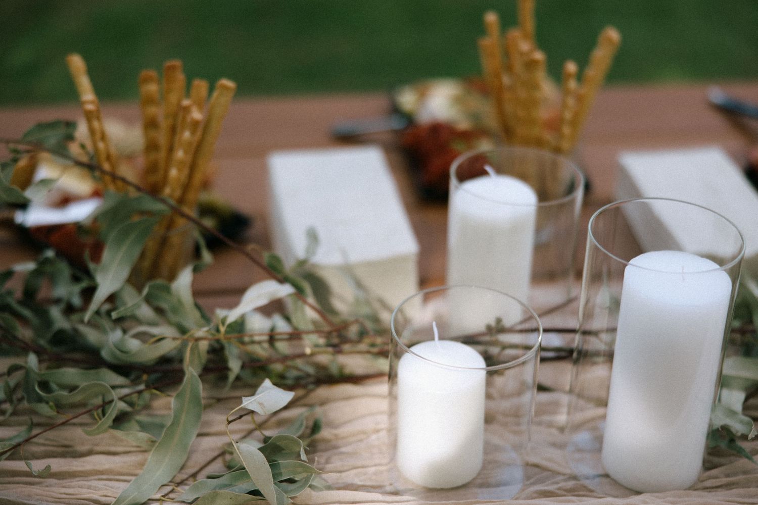 Wedding table decor featuring white candles, breadsticks and eucalyptus leaves.