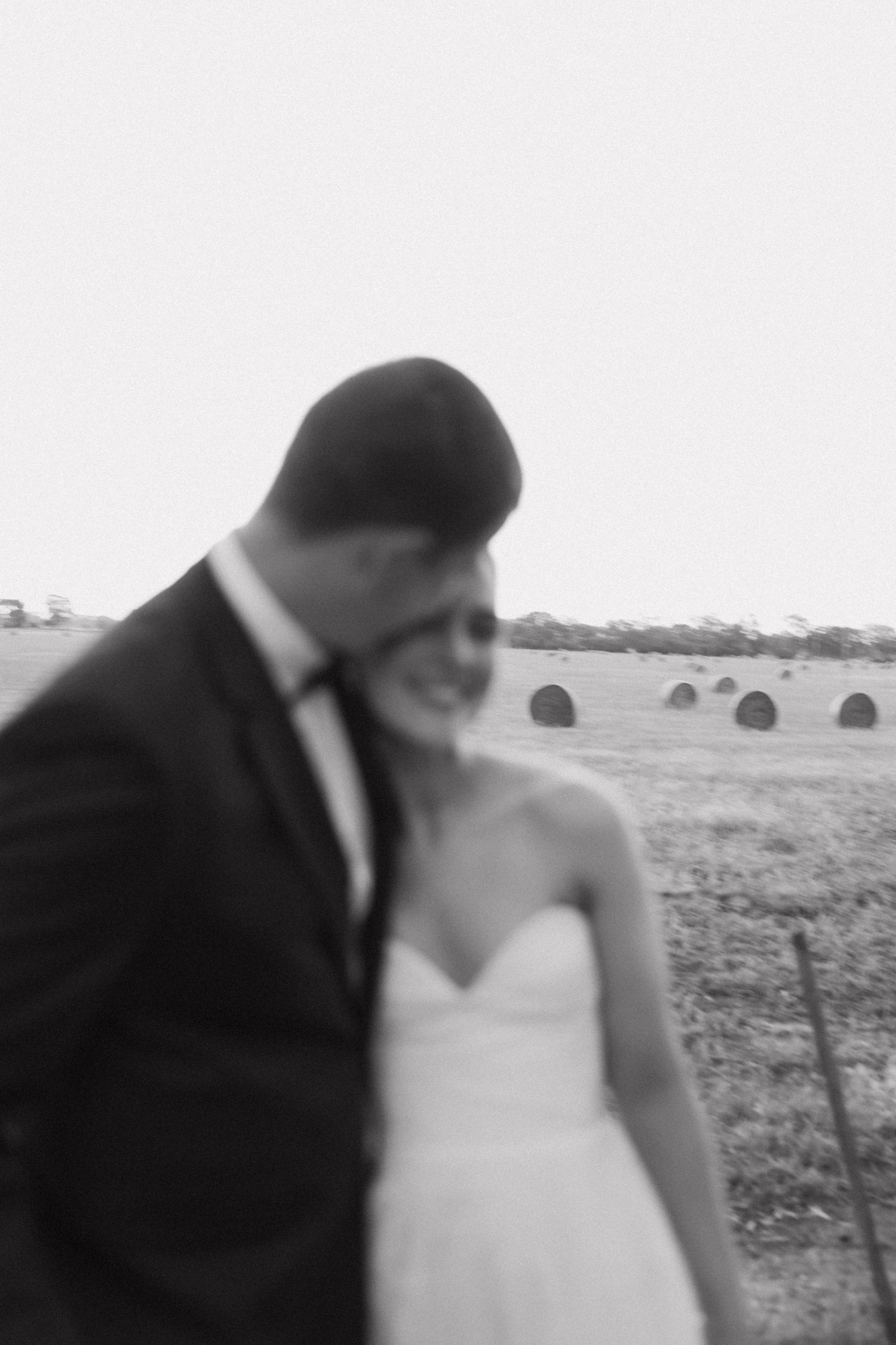 Black and white artistic wedding photo with hay bales visible in the background.