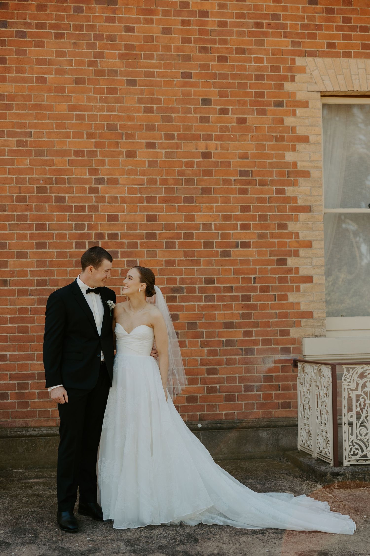Newlywed couple shares an intimate moment against rustic brick wall at their wedding ceremony.