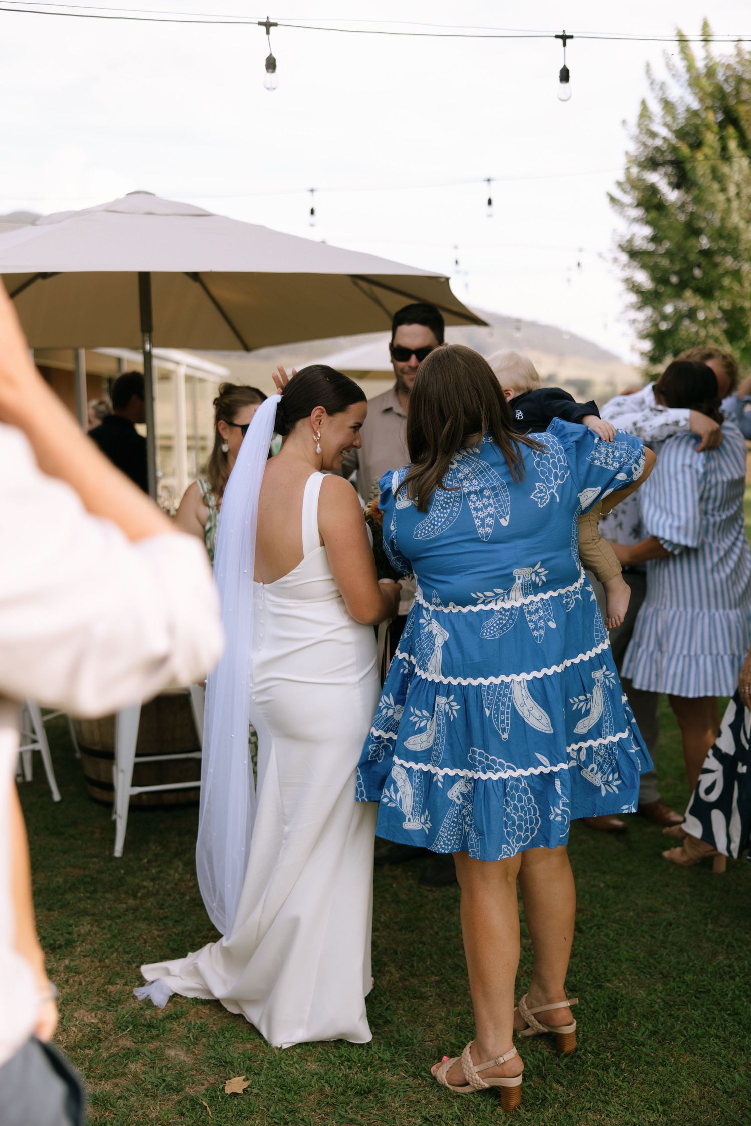 Wedding reception guests dancing outdoors under a tent on a sunny day.