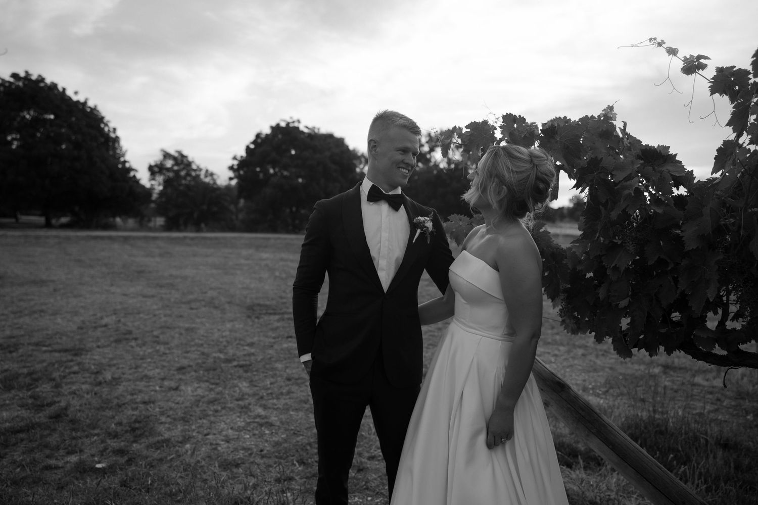 Black and white wedding photo showing couple in formal attire laughing together in an outdoor field.