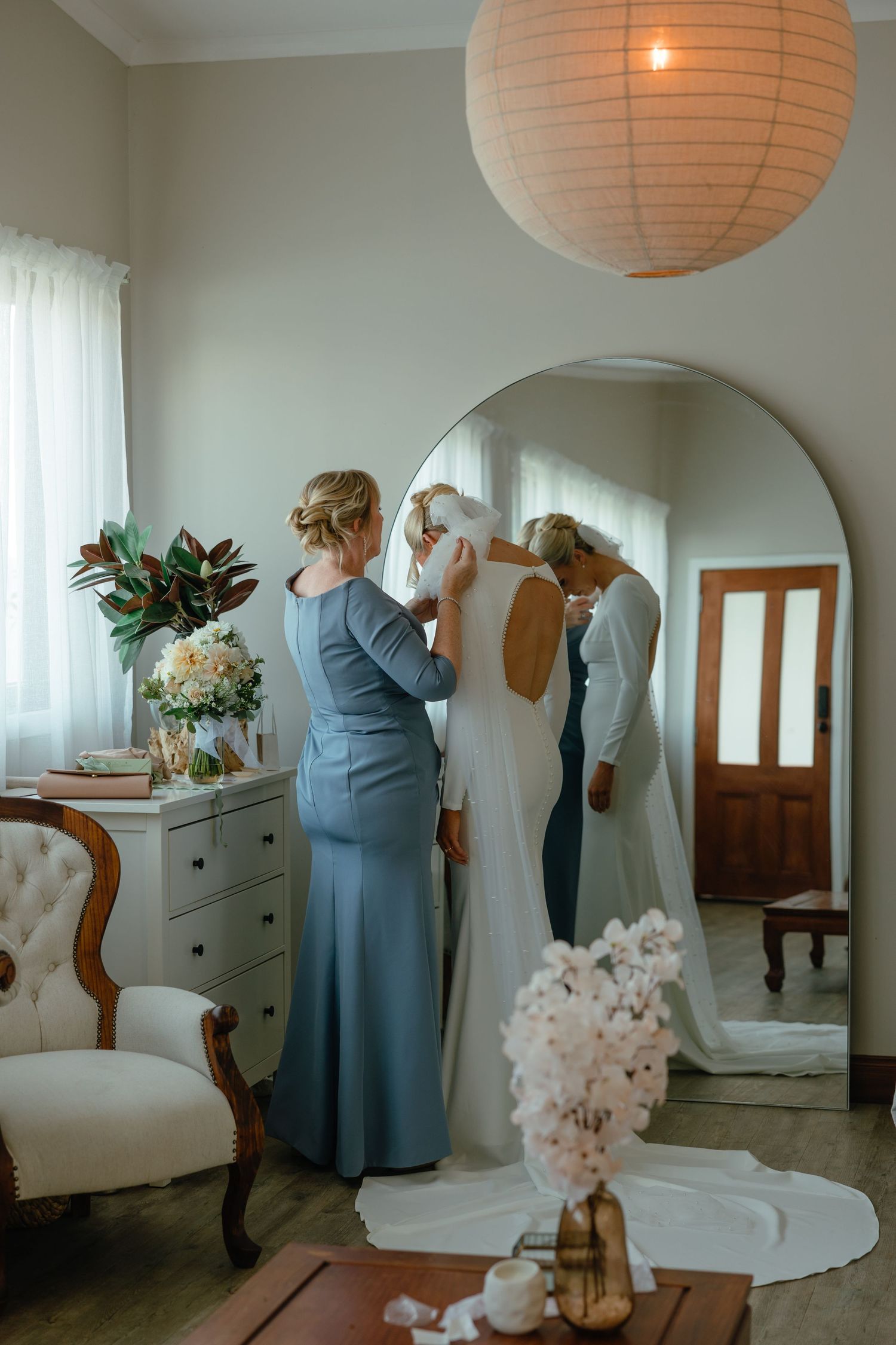 Final wedding dress adjustments in room with peach paper lantern and vintage decor.