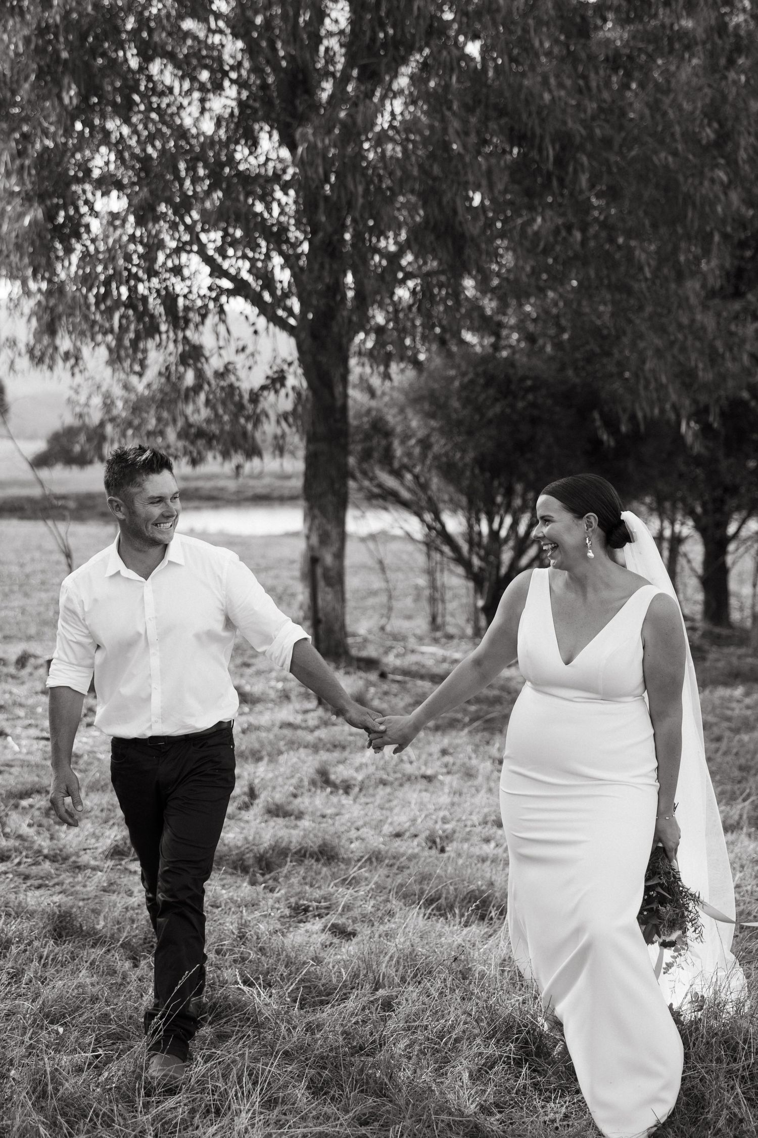 Black and white photo of couple walking together in field with trees.