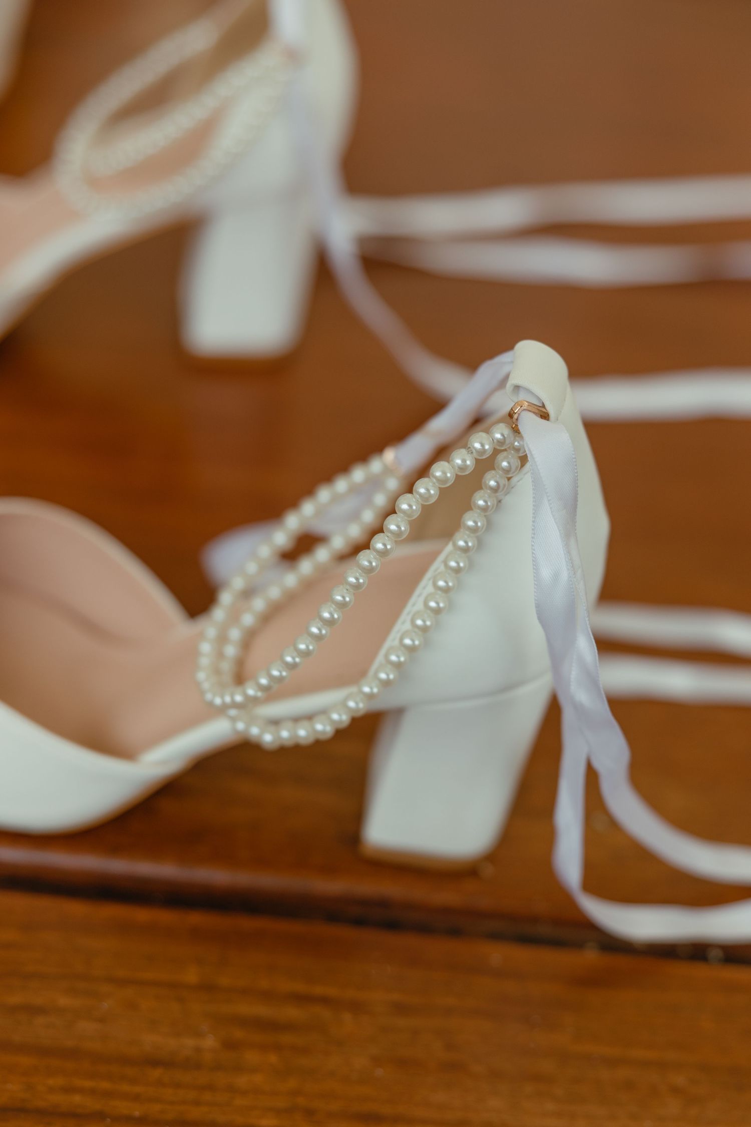 White bridal shoe with pearl details and ribbons on wooden surface.