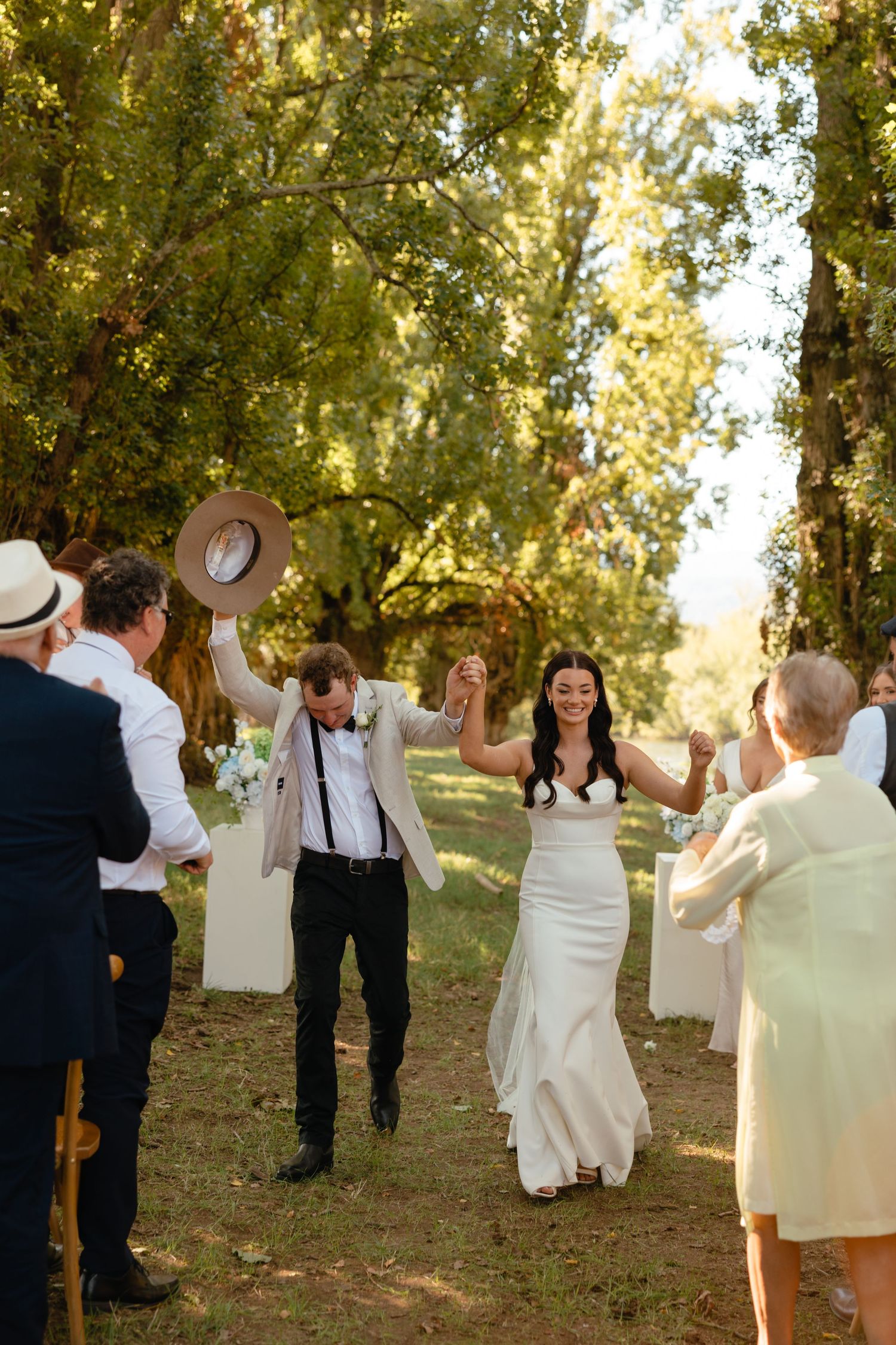 Joyful wedding guests dancing and celebrating outdoors among trees during golden hour.
