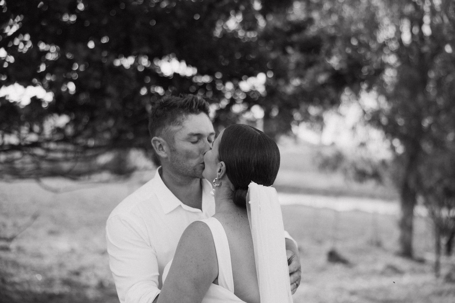 An intimate black and white portrait of newlyweds sharing a tender moment in a garden setting.