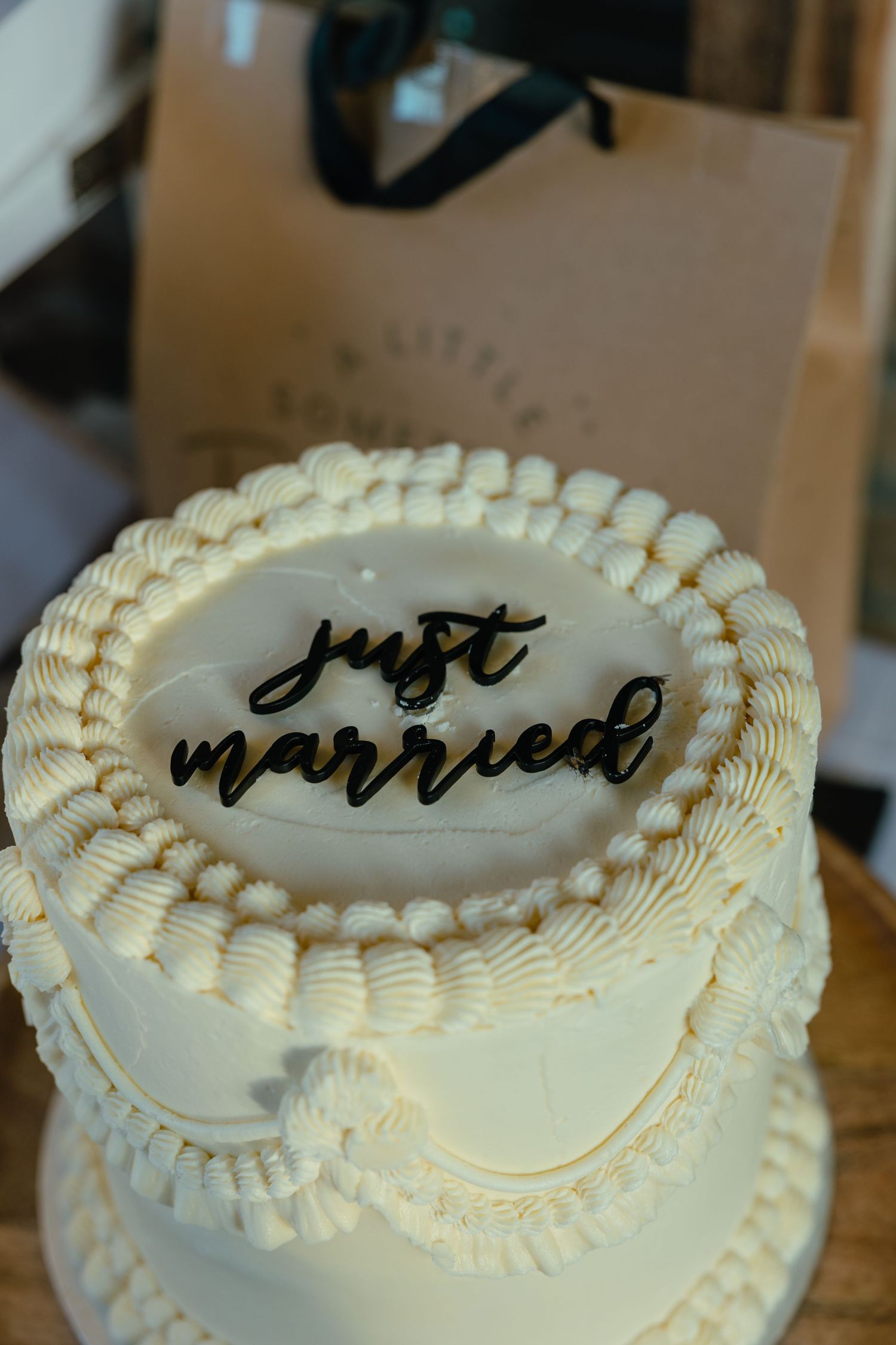 White two-tiered wedding cake decorated with piped frosting and 'just married' written in elegant black script on top.