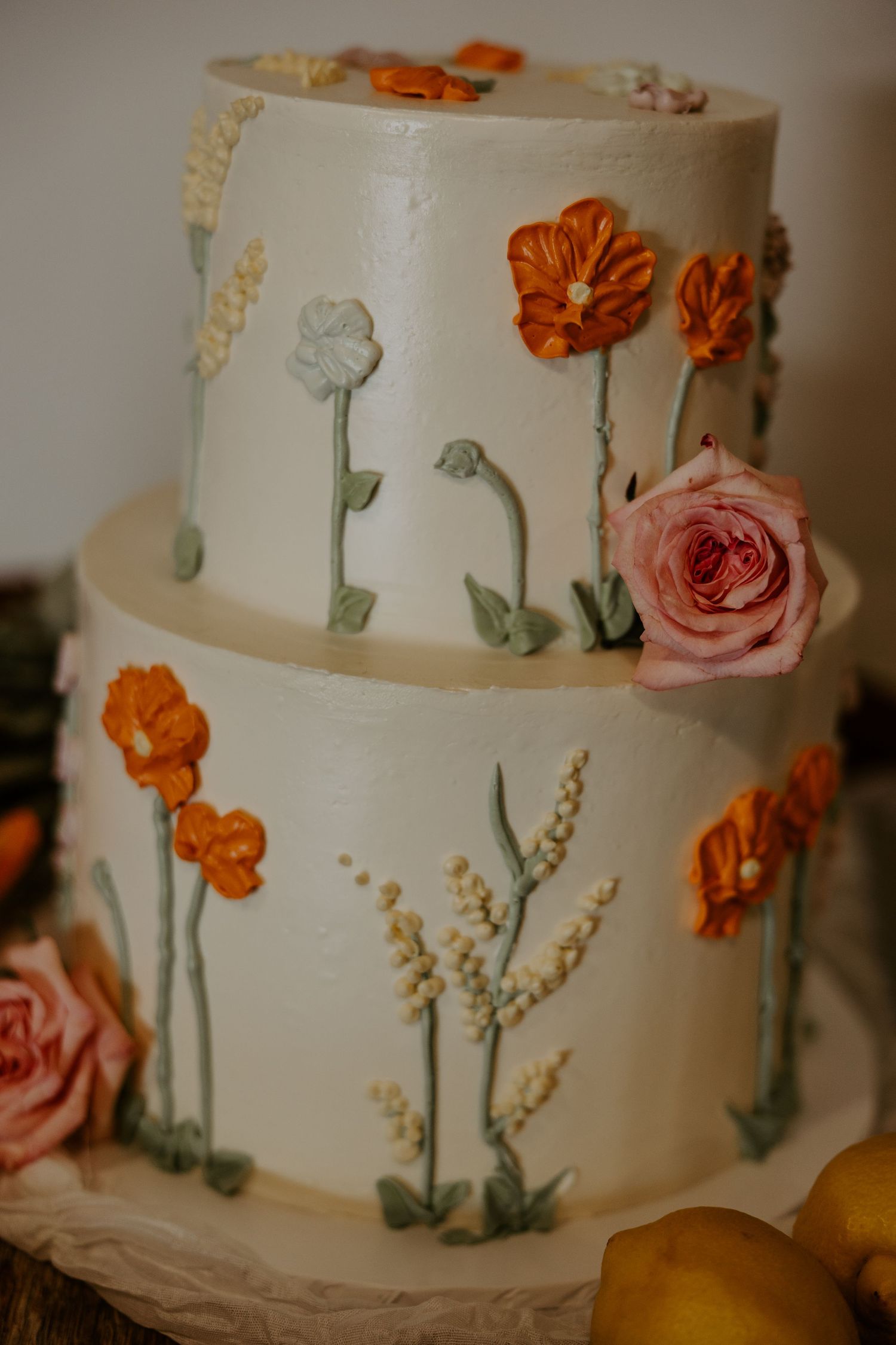 Two-tier white wedding cake decorated with orange and pink sugar flowers and delicate floral stems.