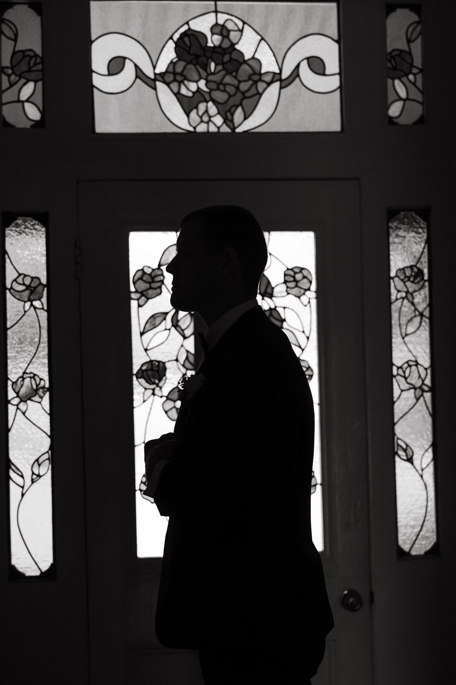 Silhouette stands in front of door with decorative stained glass panels featuring floral patterns in dramatic black and white contrast.