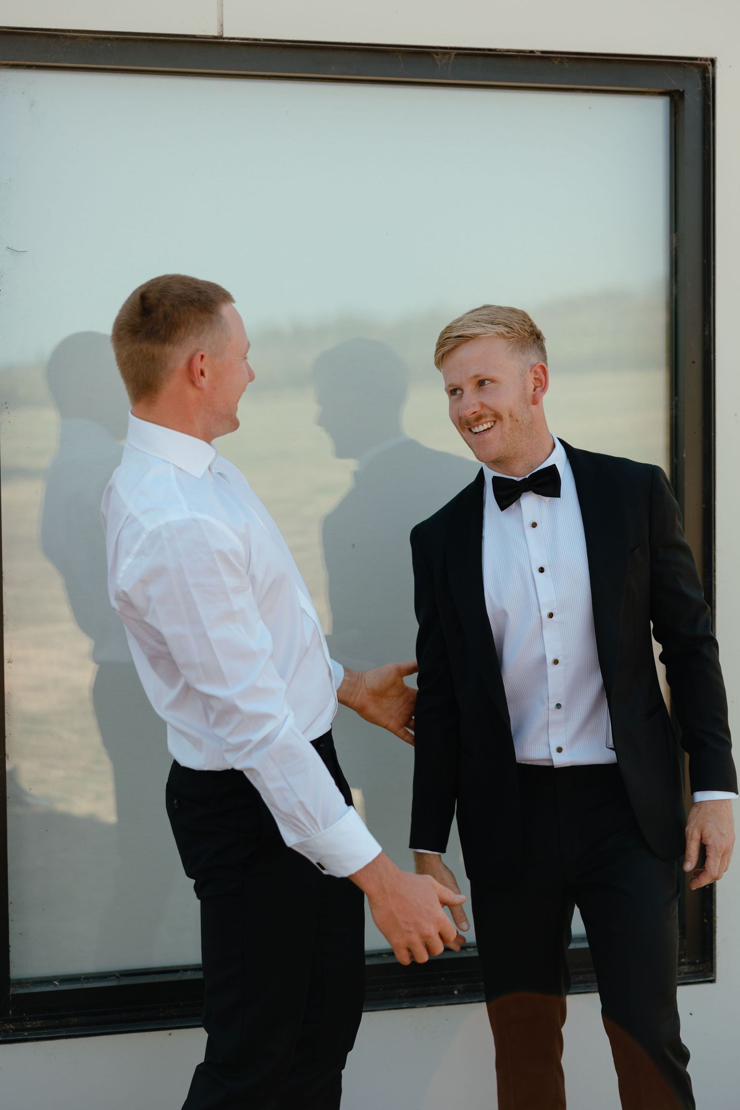 Two people in formal attire share a candid moment in front of a window.