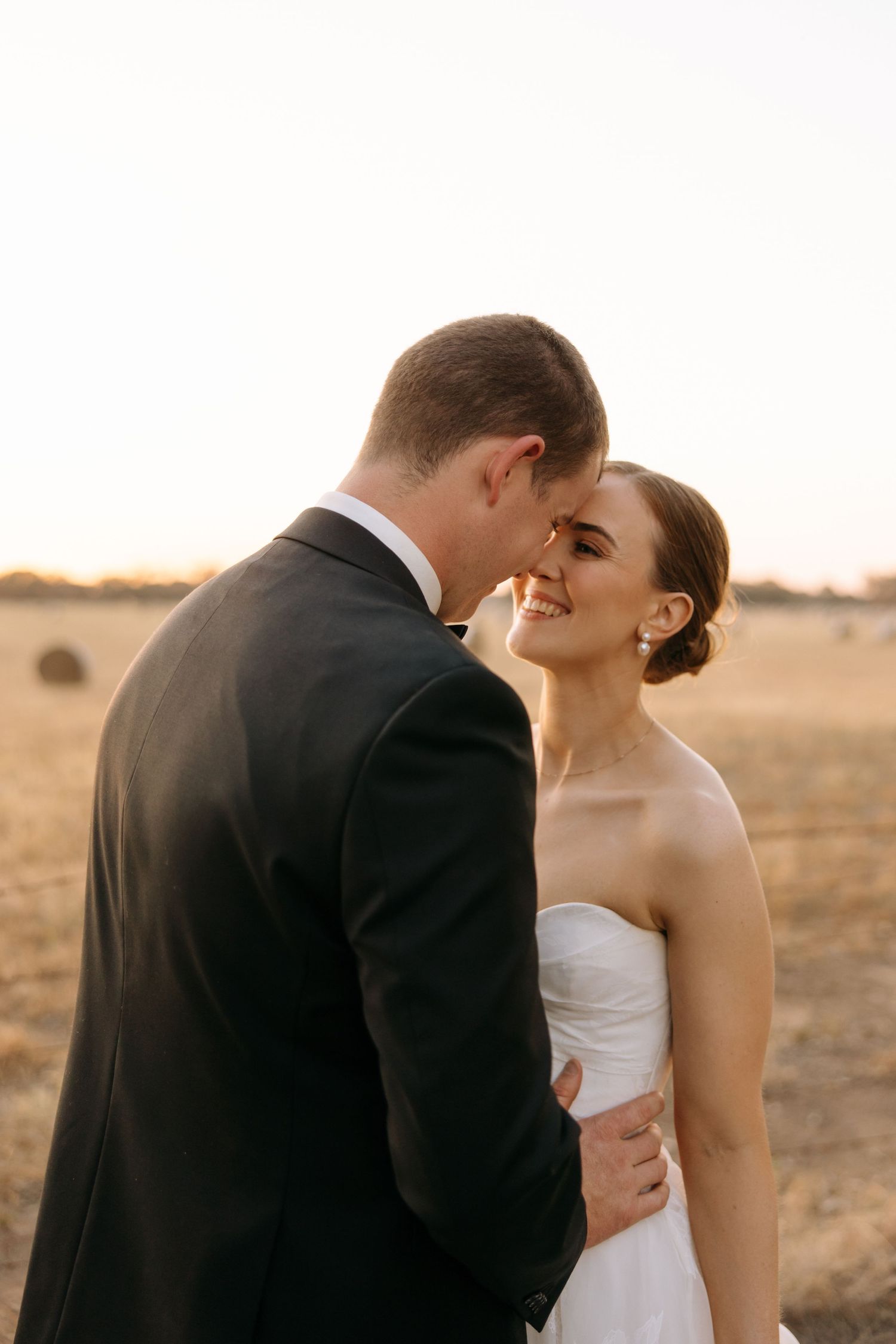 Romantic sunset portrait of newlyweds embracing in an open field.