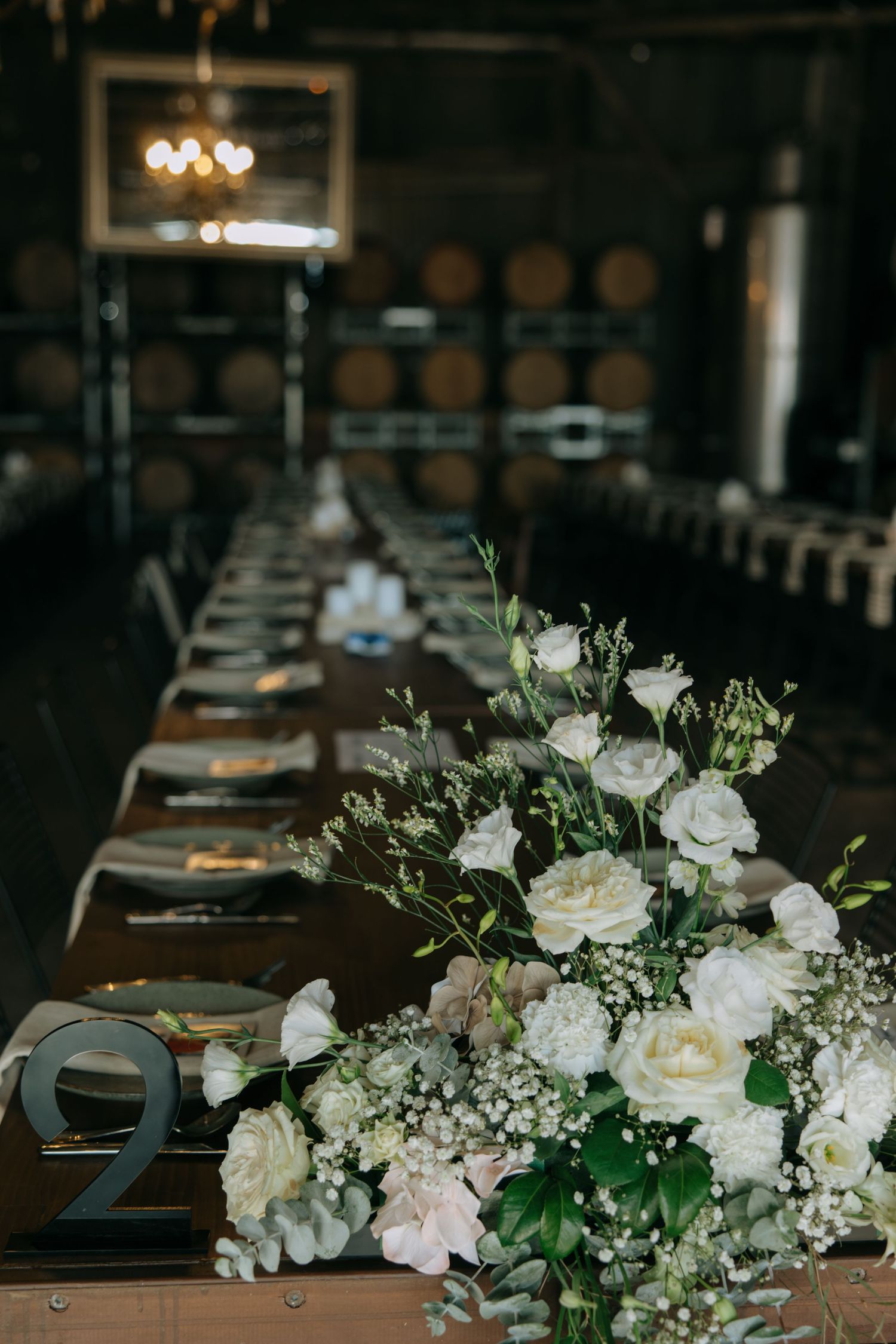 Elegant wedding table setting with white rose centerpiece and table numbers.