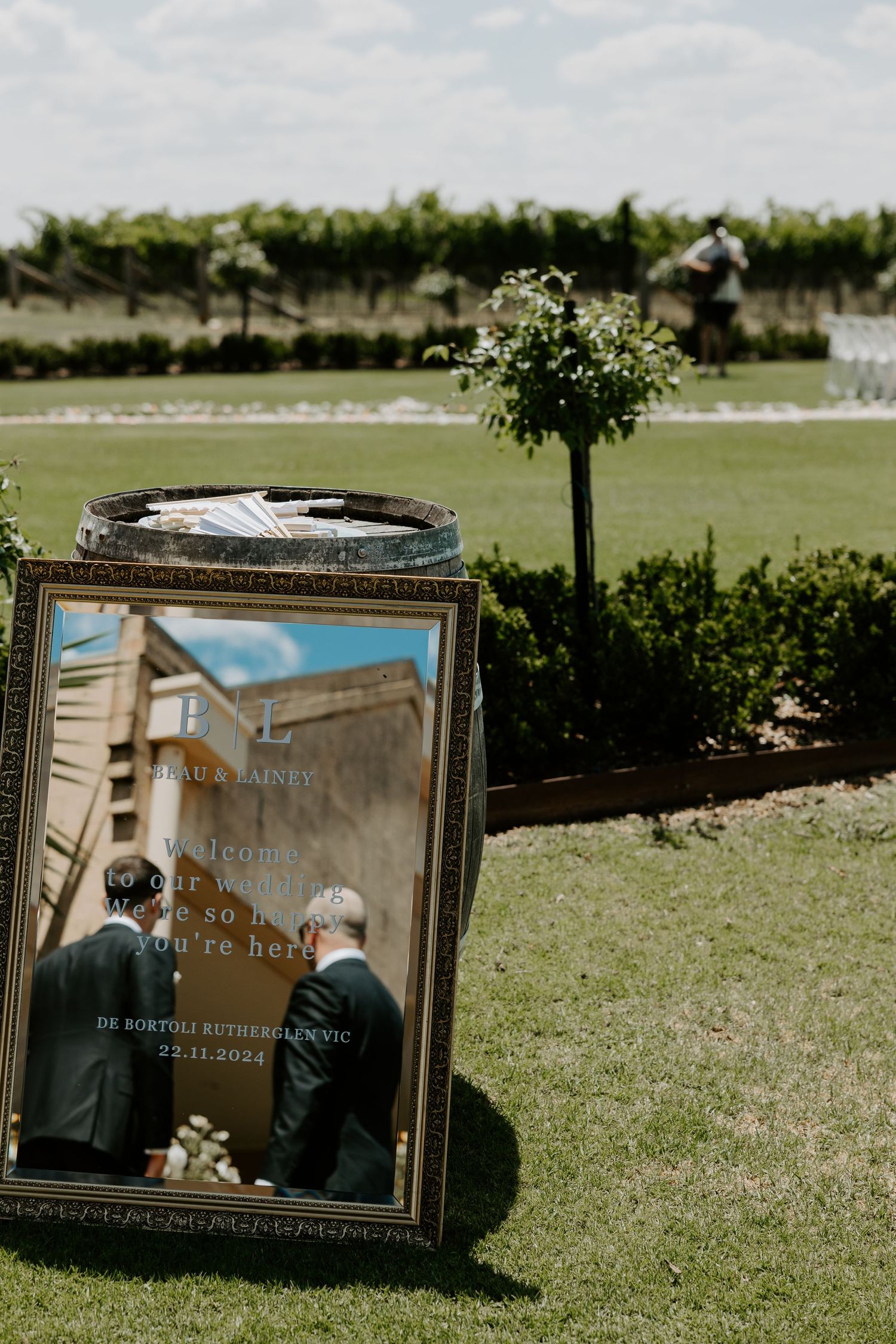 Memorial photo frame displayed on grass at an outdoor wedding ceremony with decorative greenery.