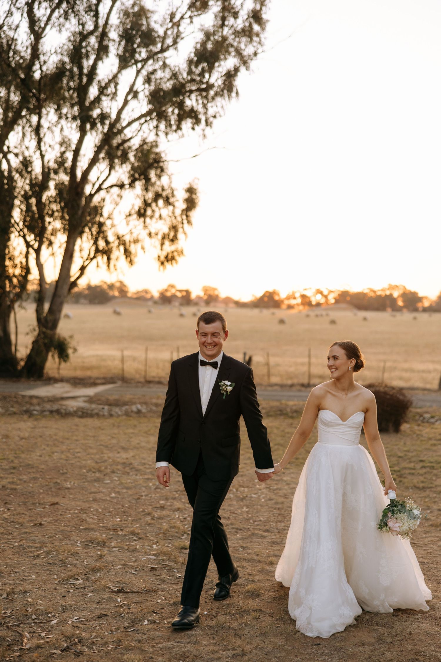 Newlyweds walking together at sunset in a rustic countryside setting.