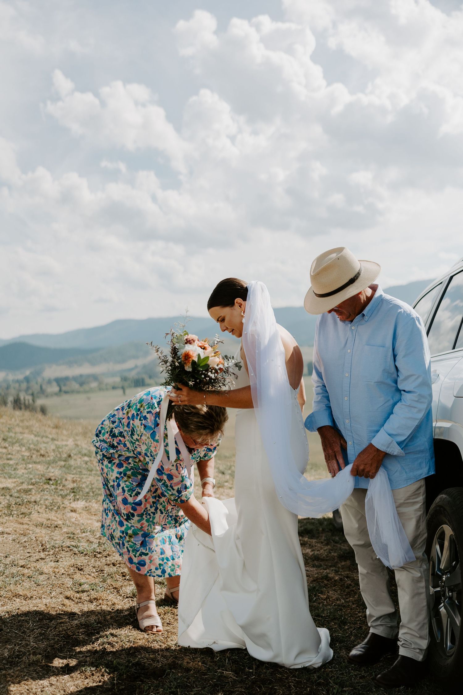 Wedding party helping with bride's dress against mountainous backdrop.