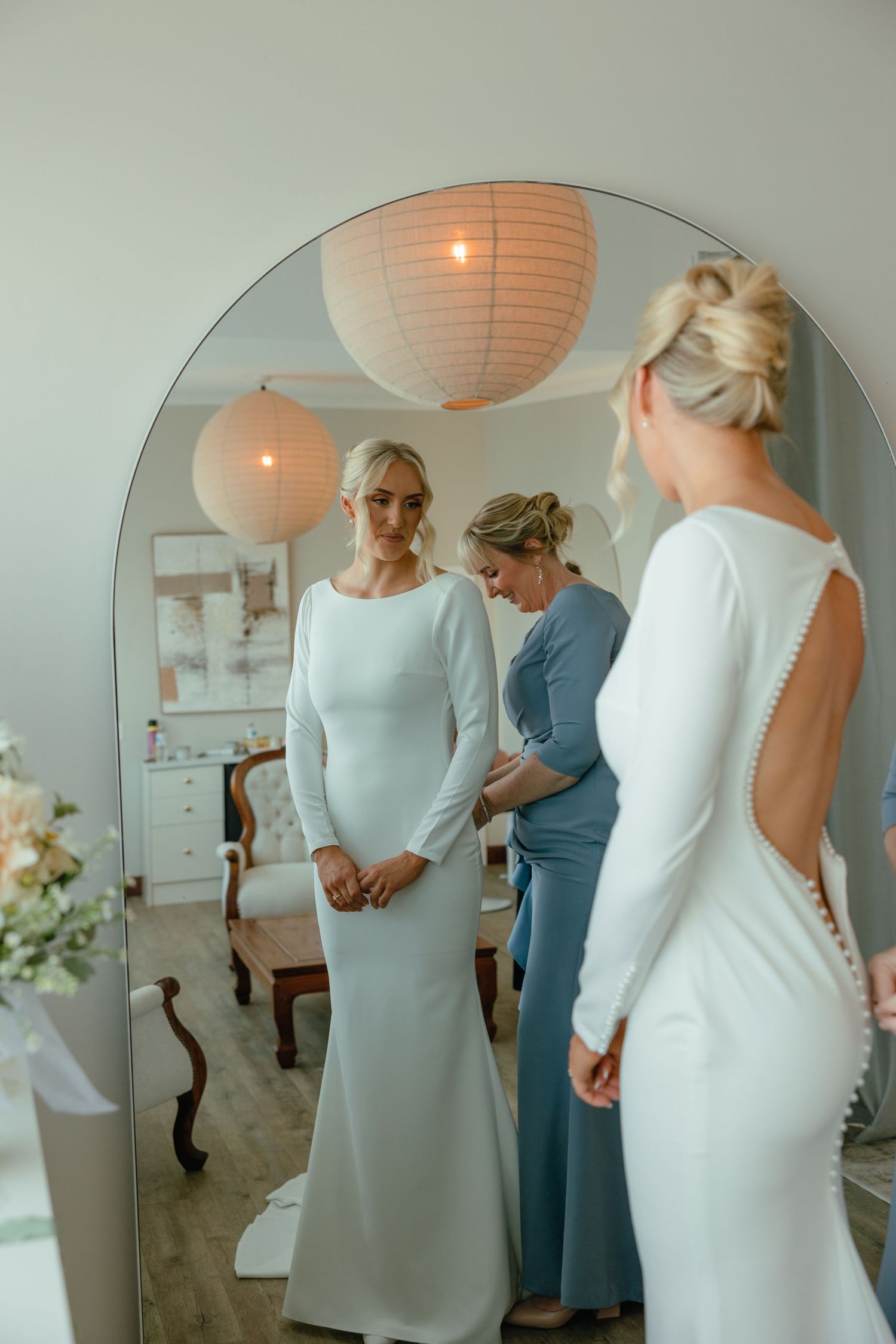 Modern bridal fitting scene with peach paper lanterns and arched mirror.